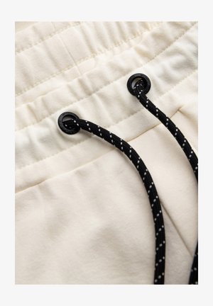 Tissu de couleur crème avec une texture douce, caractérisé par une taille froncée et un cordon noir avec des pois blancs.