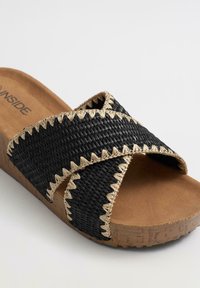 Sandalia deslizante negra de tejido con tiras entrecruzadas, que presenta un diseño de puntadas en zigzag beige y una suela marrón texturizada. Plantilla suave para mayor comodidad.