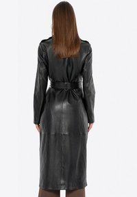 Abrigo de trench de cuero negro con mangas largas, cintura ceñida, silueta ajustada y textura suave, con detalles de costura en la parte posterior.