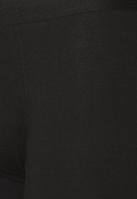 Schwarze Leggings aus glattem, dehnbarem Material. Sie verfügen über einen weichen, breiten Bund und ein eng anliegendes Design mit flachen Nähten.