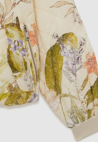 Veste bombardier matelassée avec des motifs floraux en vert, violet et rose sur un fond beige. Comprend une poche zippée et des poignets côtelés.