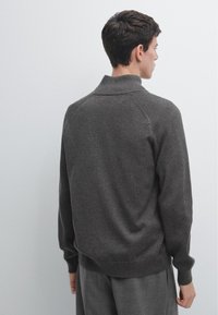 Donkergrijze gebreide trui met hoge kraag, geribbelde structuur en lange mouwen, met een losse pasvorm en een effen achterzijde.