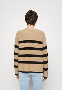 Beige gebreide trui met brede zwarte strepen, ronde halslijn en lange mouwen, gecombineerd met lichtblauwe spijkerbroek. Gelaagde stof.