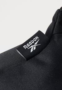 Fekete szövet táska, texturált felülettel, fehér Reebok logós címkével a szélén. Kompakt kialakítás, sport vagy hétköznapi használatra is alkalmas.