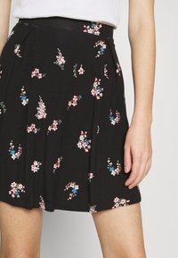 Zwarte bloemenrok van lichtgewicht stof, met rozen- en blauwe bloemendessins, plooien en een tailleband.