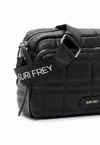 Sac à épaule noir matelassé avec fermeture à glissière, sangle réglable et détail de logo. Présente une texture lisse et une forme rectangulaire.