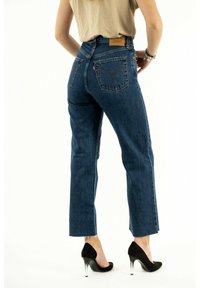 Jean bleu taille haute avec une silhouette droite, en denim délavé et avec des coutures contrastantes, associés à des chaussures à talons hauts noires.