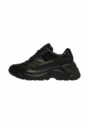 Sneakers neri con suola spessa, caratterizzati da texture a rete e liscia, dettagli dorati e un logo di marca ben visibile di lato.