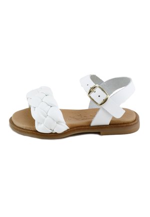 Sandalia plana blanca con tira frontal trenzada, correa ajustable en el tobillo con hebilla dorada y suela acolchada color cuero claro.