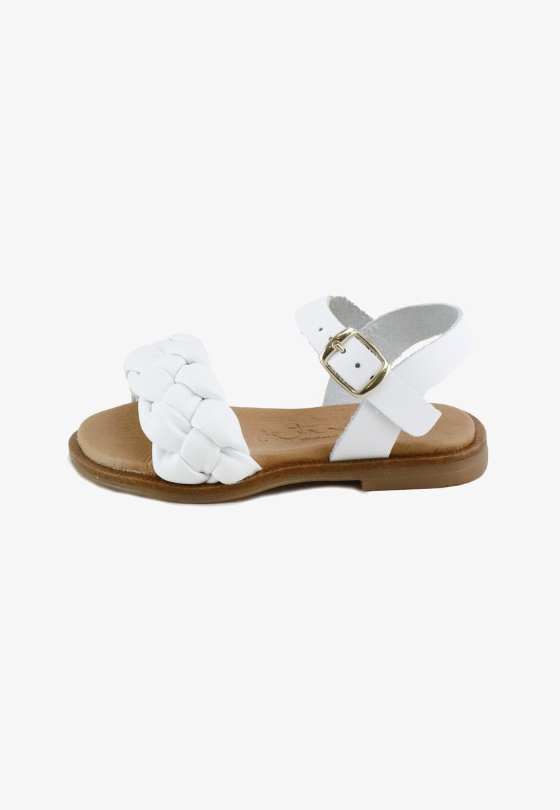 Sandalia plana blanca con tira frontal trenzada, correa ajustable en el tobillo con hebilla dorada y suela acolchada color cuero claro.