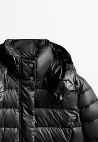 Sort polstret jakke med høj krave, glat stof, trykknapper og quiltet design med horisontale sektioner.