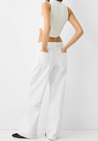 Jeans blancos de pierna ancha con grandes bolsillos traseros, combinados con un top corto texturizado blanco con canalé vertical.
