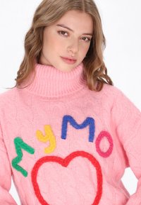Pulover roz din tricot cu guler înalt, decorat cu litere din fetru colorate și un design cu inimă în roșu, albastru, verde și galben.