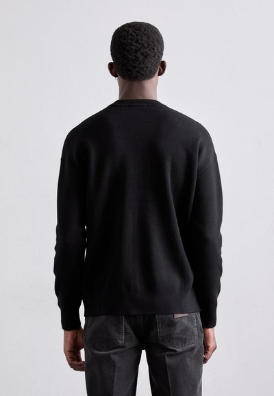Pull noir en laine avec un col rond, des manches longues et une coupe légèrement ample. Texture lisse, sans motifs visibles ni détails métalliques.