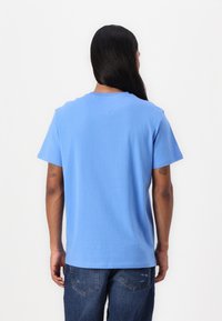 T-shirt en coton bleu à manches courtes avec un col rond, détail de couture au dos et coupe décontractée, associé à un jean en denim.