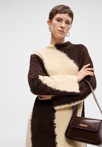 Καφετί και κρεμ πουλόβερ πλεκτού με υφή, φαρδιά μανίκια και ψηλό γιακά, συνδυασμένο με μια μικρή καφέ δερμάτινη τσάντα ώμου.