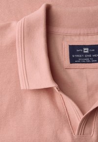Ljust rosa strukturerad polo med ribbad krage och en marinblå etikett med texten "Street One Men" på insidan av kragen.