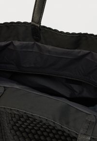 Μαύρη υφαντή τσάντα ώμου με λείες λεπτομέρειες από δέρμα. Το εσωτερικό διαθέτει ματ φινίρισμα και ασφαλές τσεπάκι με φερμουάρ. Ανθεκτικές λαβές για εύκολη μεταφορά.