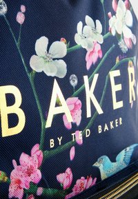 Geantă cu un model floral, având flori roz și albe pe un fundal albastru închis, cu textul auriu "BAKER" și o ilustrație de pasăre albastră.