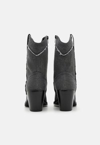 Botas de tobillo de denim gris con puntera afilada y detalles deshilachados. Presentan un tacón bajo y grueso, además de un cierre lateral con cremallera para ponerlas y quitarlas fácilmente.