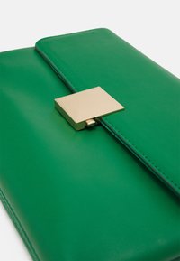 Clutch de cuero verde con una textura suave, que presenta un broche metálico dorado y líneas limpias, exhibiendo un diseño minimalista.