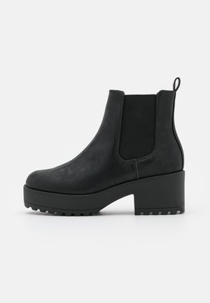 Bottine noire en cuir lisse avec des panneaux latéraux élastiques, une languette à l'arrière et un talon épais avec une semelle texturée pour une meilleure adhérence.