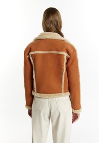 Bruine shearling jas met een gestructureerde afwerking, voorzien van een fluffy kraag en randen, en contrasterende stikdetails, gezien vanuit de achterkant.