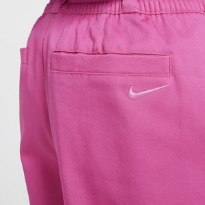 Ružové športové nohavice s ľahkým materiálom, s zadnou vreckom a vyšívaným bielym logom Nike na pravej strane. Elastický pás.