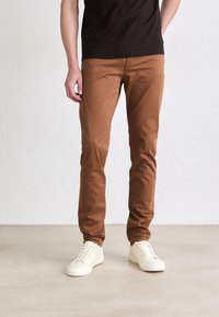 Barna pamut chinos nadrág, slim fit szabással, sima textúrával és elülső zsebekkel, világosbézs sportcipővel párosítva.