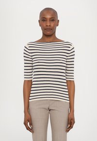Top en tricot rayé crème et marine, avec un col bateau et des manches courtes. Texture douce, design ajusté, assorti à un pantalon gris clair.