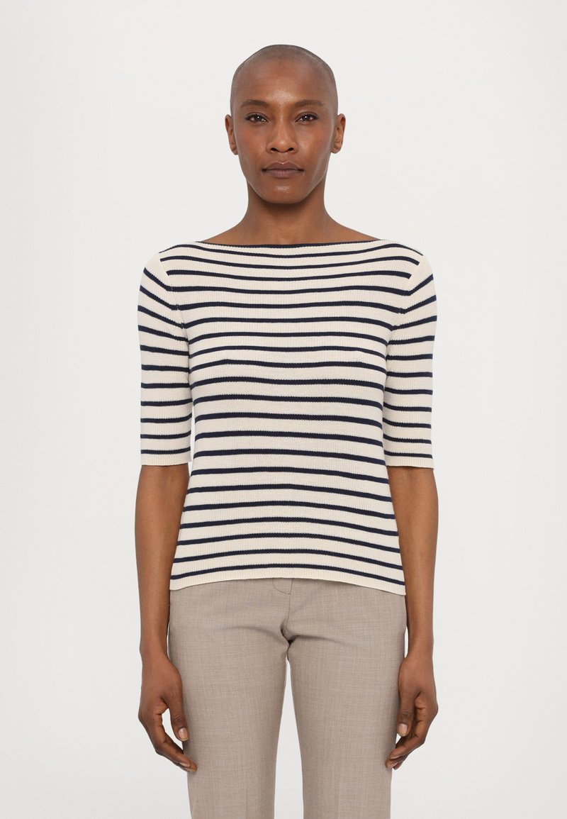 Top en tricot rayé crème et marine, avec un col bateau et des manches courtes. Texture douce, design ajusté, assorti à un pantalon gris clair.