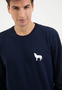 Granatowy sweter z mieszanki bawełny z okrągłym dekoltem, z białą sylwetką wyjącego psa na lewej piersi.