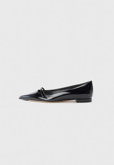 Chaussure plate en cuir verni noir avec un bout pointu, une petite lanière décorative et un petit talon carré. Texture lisse et design épuré.