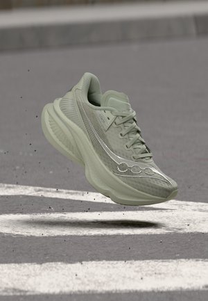 Chaussure de sport vert clair avec une semelle épaisse flottant au-dessus d'une route asphaltée avec des marquages blancs peints.