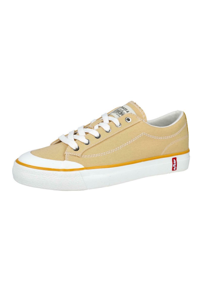 Zapatilla baja de lona beige con cordones blancos, suela gruesa de goma blanca, franja amarilla y pequeña etiqueta roja con el logo de Levi's en el lateral.