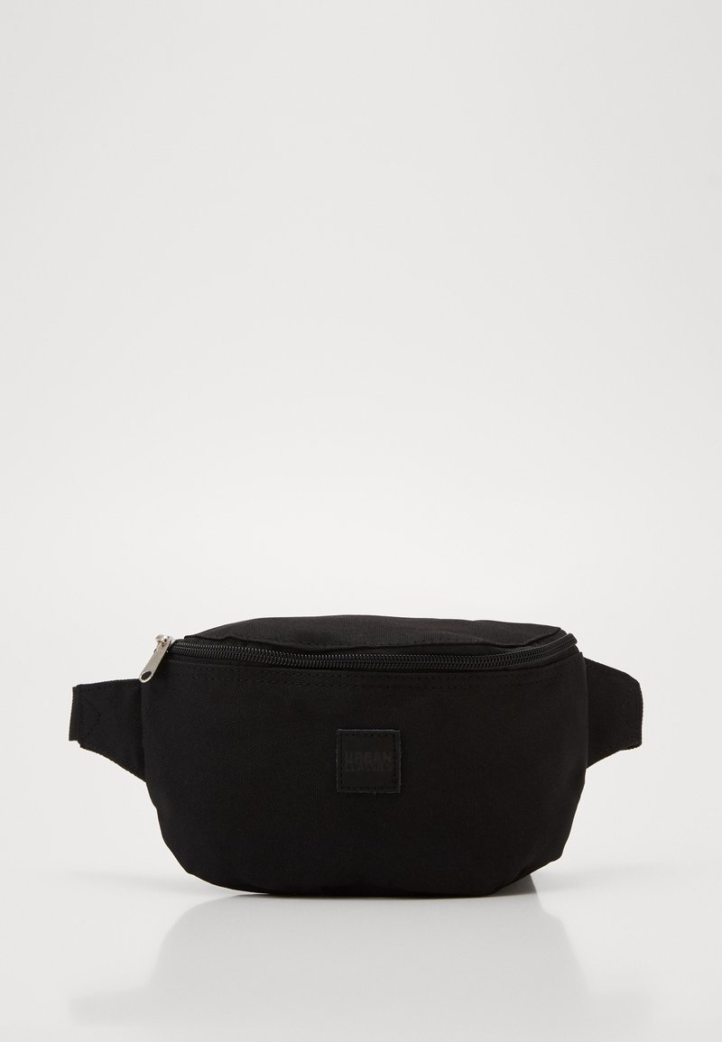 Sac banane en tissu noir avec une fermeture éclair supérieure et des sangles latérales réglables sur fond blanc.