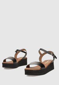 Sandalias de cuña negras con correas anchas y hebilla en el tobillo, que presentan una parte superior texturizada y una suela de plataforma en capas en un marrón contrastante.