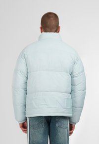 Šviesiai mėlynas pūkinis švarkas su aukštu apykakle ir iškilniu „KANI“ logotipu nugaros pusėje. Pasižymi siūtu tekstūra ir didesniu dydžiu.