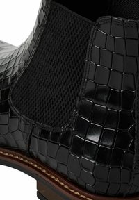 Botte cheville en cuir noir à texture crocodile, avec panneau latéral élastique, semelle marron cousue et petit talon empilé.