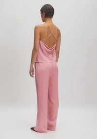 Roze satijnen camisole met dunne kruislings gekruiste bandjes en een gedrapeerde achterkant, gecombineerd met bijpassende losse broek. Glad textuur, minimalistisch ontwerp.