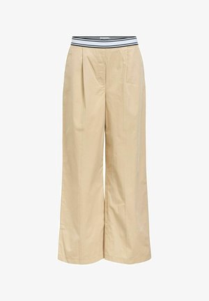 Pantalons larges beiges avec une ceinture élastique à rayures noires et blanches, présentant des plis à l'avant et une texture en coton lisse.