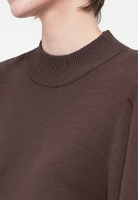 Brun strikket sweater med en høj ribbestrikning og glat tekstur, med en tætsiddende pasform og subtile skulderdetaljer.