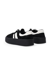 Czarne zamszowe sneakersy na platformie z białymi skórzanymi akcentami, okrągłym noskiem, płaskimi sznurówkami i chropowatą gumową podeszwą o wyraźnej wysokości.