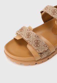 Sandalo con suola color cuoio e cinturini in pelle, dotato di cinturini regolabili in tessuto beige con motivo monogramma marrone e suola testurizzata.
