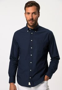 Marineblaues Hemd mit langen Ärmeln, einer einzigen Brusttasche und hellen Knöpfen; aus glattem Stoff mit normaler Passform gefertigt.
