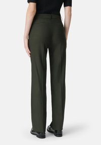 Pantaloni su misura verde scuro con gamba dritta, texture liscia, passanti per cintura e due tasche posteriori. Indossati con scarpe nere.