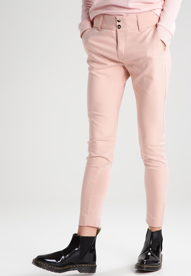 Pantalon rose clair sur mesure avec une texture lisse, doté d'une coupe ajustée, de deux poches avant, et de bottines noires aux chevilles.