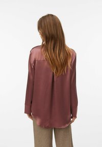 Langærmet satinbluse i mauve med buet kant, detalje med rygplys og afslappet pasform. Glat tekstur, ingen synlige mønstre eller accenter.