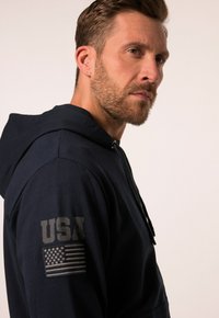 Navy hoodie with a relaxed fit, featuring hood, drawstrings, and USA graphic with flag on the left sleeve.  Soft texture and casual design.