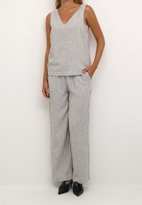 Top sans manches rayé avec un décolleté en V, associé à un pantalon à jambes larges. Les deux en tissu léger avec des rayures verticales bleu marine et blanches.